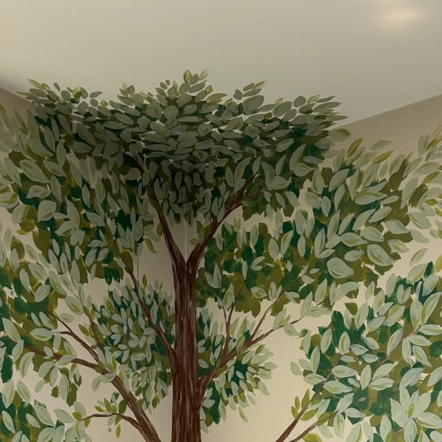 Painted tree with a canopy of layered green leaves spreading across a nursery wall and into the corner